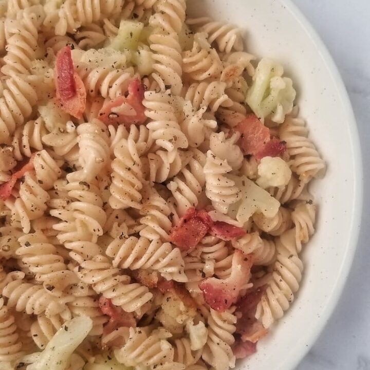 close up of a bowl of curly brown rice pasta with bacon and cauliflower pieces