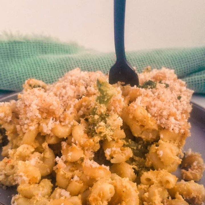 fork piercing into a generous slice of vegan mac and cheese baked with broccoli and breadcrumbs on a plate