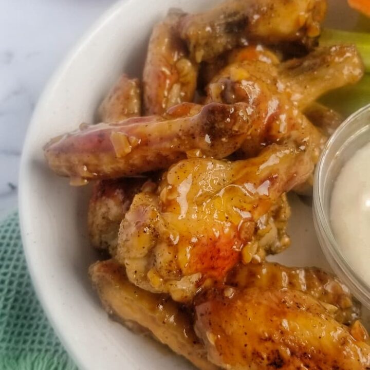 side view of bowl of honey garlic chicken wings with homemade honey garlic sauce in a bowl with a rubber spatula in the background