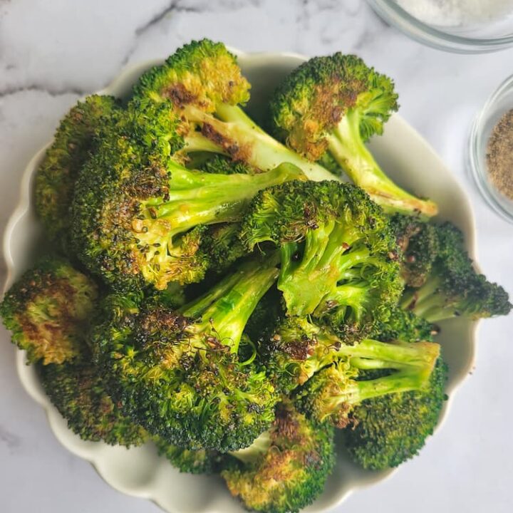 bowl of roasted broccoli, ramekins of salt and pepper on the side