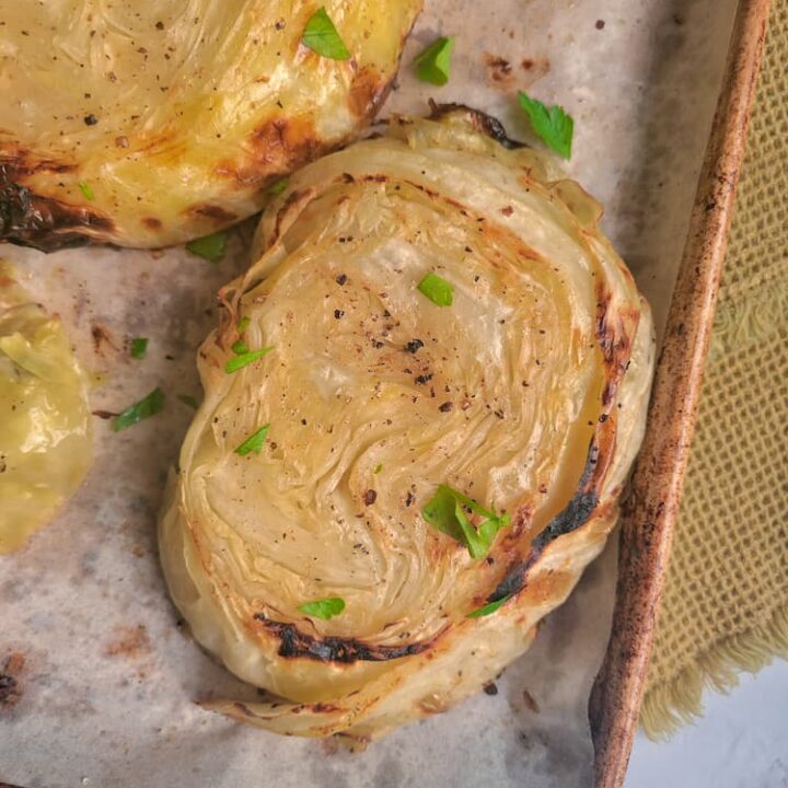 grilled cabbage steaks on a parchment lined sheet pan garnished with fresh chopped parsley