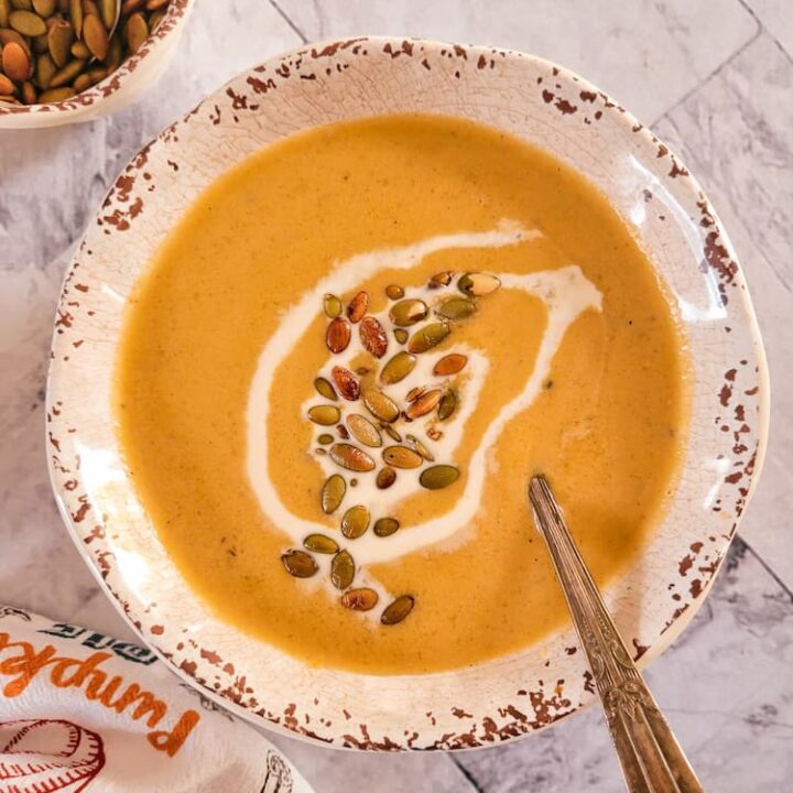 bowl of pumpkin soup topped with toasted pepitas and a heavy cream swirl