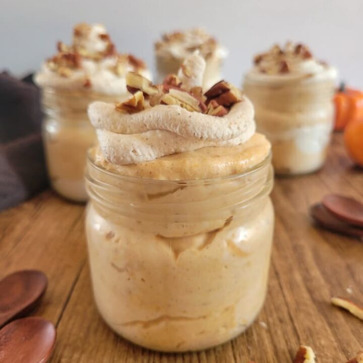 4 jars of pumpkin mousse topped with pecans and whipped cream