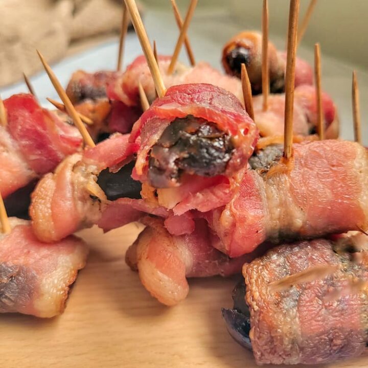 bacon wrapped dates with toothpicks piled onto a cutting board