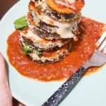 plate of low fodmap eggplant parmesan rounds stacked up on a plate with lots of tomato sauce, fresh basil, lactose free cheese and gluten free breadcrumbs