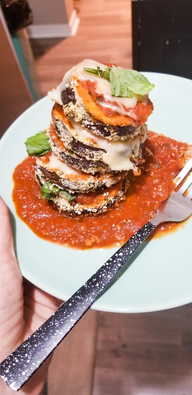 plate of low fodmap eggplant parmesan rounds stacked up on a plate with lots of tomato sauce, fresh basil, lactose free cheese and gluten free breadcrumbs