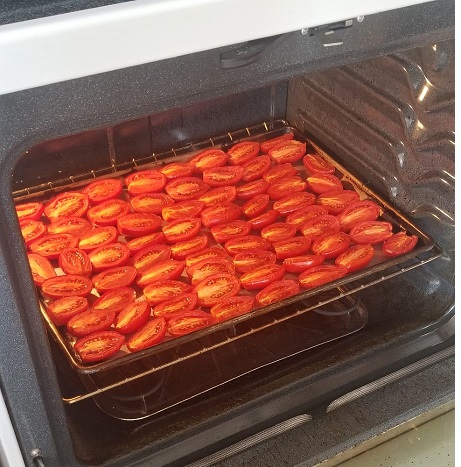 a large sheet pan on the lowest oven rack displaying several rows of halved san Marzano tomatoes, flesh side up, showcasing the oven kick start method 