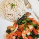 a pile of rice, surrounded by stir-fried shrimps and vegetables such as bok choy, mushrooms and carrots