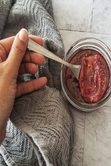 A hand holding a fork with a sun dried tomato on it, coming out of a jar of sun dried tomatoes in oil