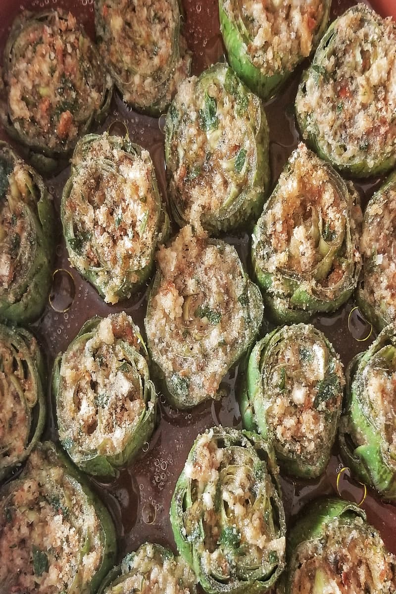 Several Italian stuffed artichokes (also known as carciofoli) sit side by side in a pan, stuffed with breadcrumbs, garlic, parsley
