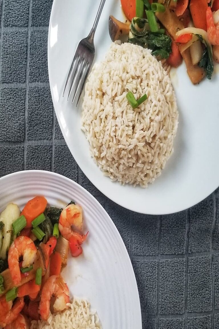 a pile of rice, surrounded by stir-fried shrimps and vegetables such as bok choy, mushrooms and carrots