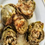 Italian stuffed artichokes (also known as carciofoli) sit side by side in a plate, stuffed with breadcrumbs, garlic, parsley (there are 5 artichokes on this plate)