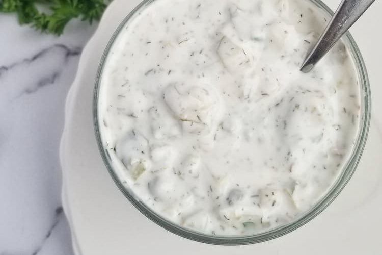 a jar of homemade tartar sauce with a spoon in it, half lemon and bunch of parsley in the backgroud