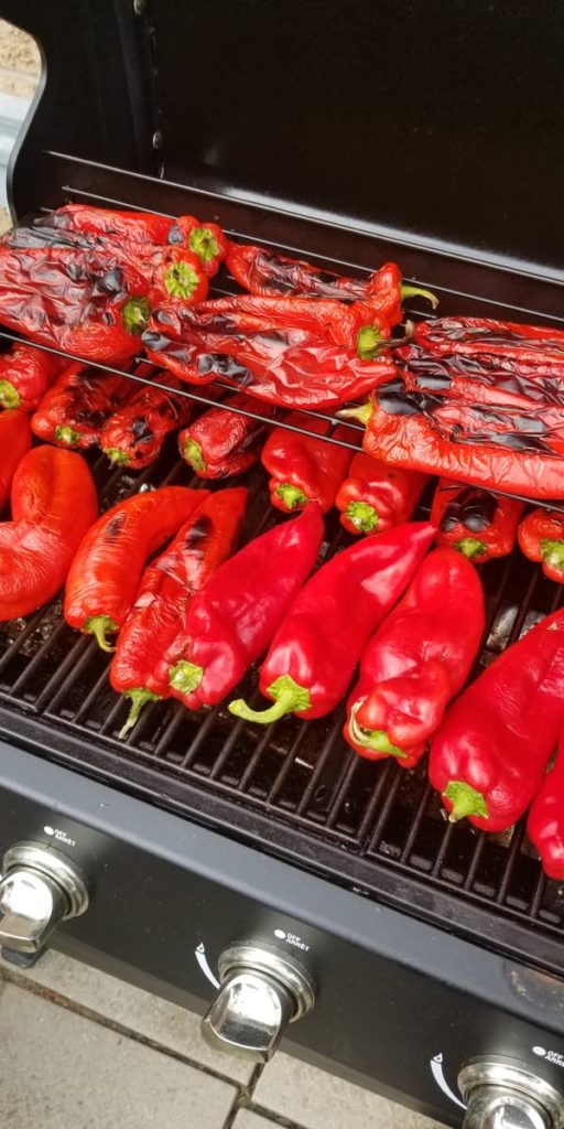 whole red peppers roasting on an open BBQ