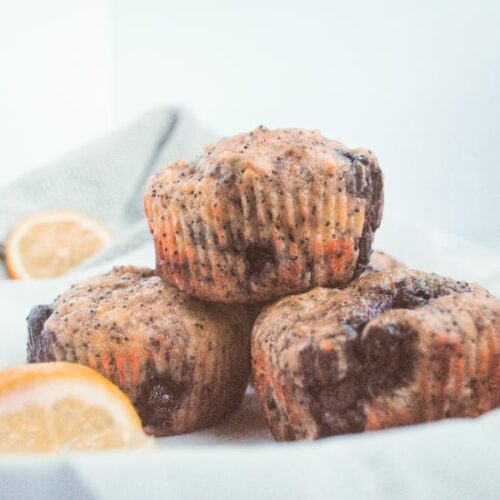 3 blueberry lemon poppyseed muffins with a slice of lemon in the background and the front