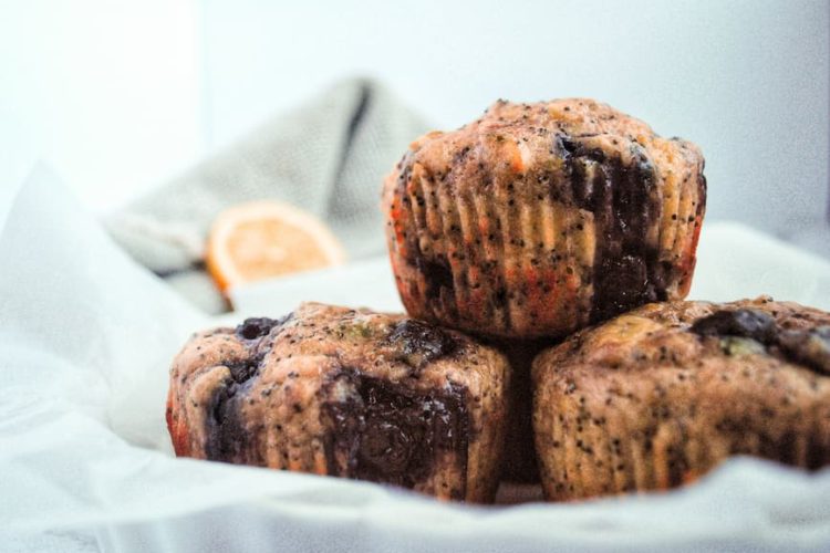 3 blueberry lemon poppyseed muffins with a slice of lemon in the background