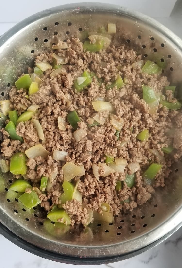 browned ground beef with sauteed green peppers and onions in a colander