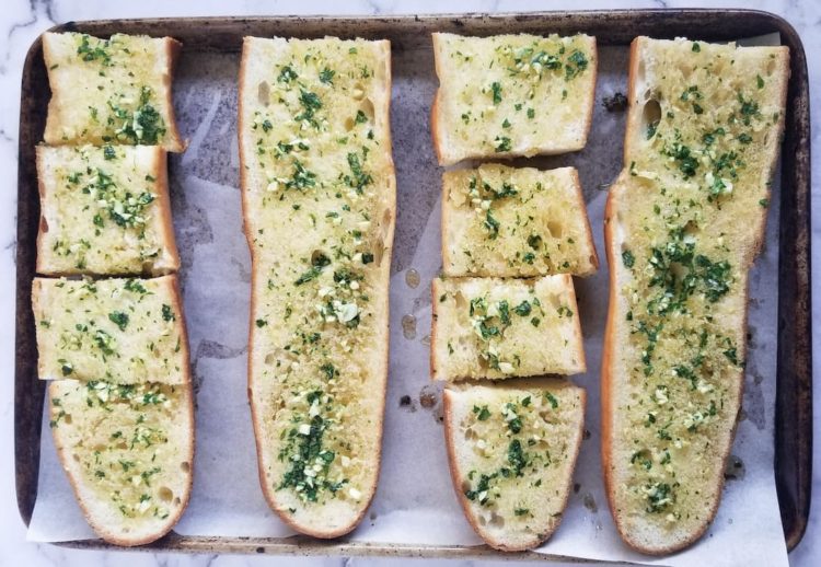 parchment lined baking sheet with four loaves of garlic bread with fresh chopped parsley and garlic