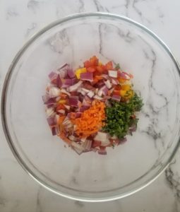 all of the ingredients for mango habanero salsa in a large glass bowl ready to be mixed - mangos, red onions, parsley, habaneros, red peppers