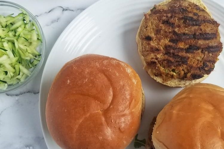 3 zucchini turkey burgers on buns, one open face, red onion sticking from one, small bowl of shredded zucchini and white dip with spoon in the background