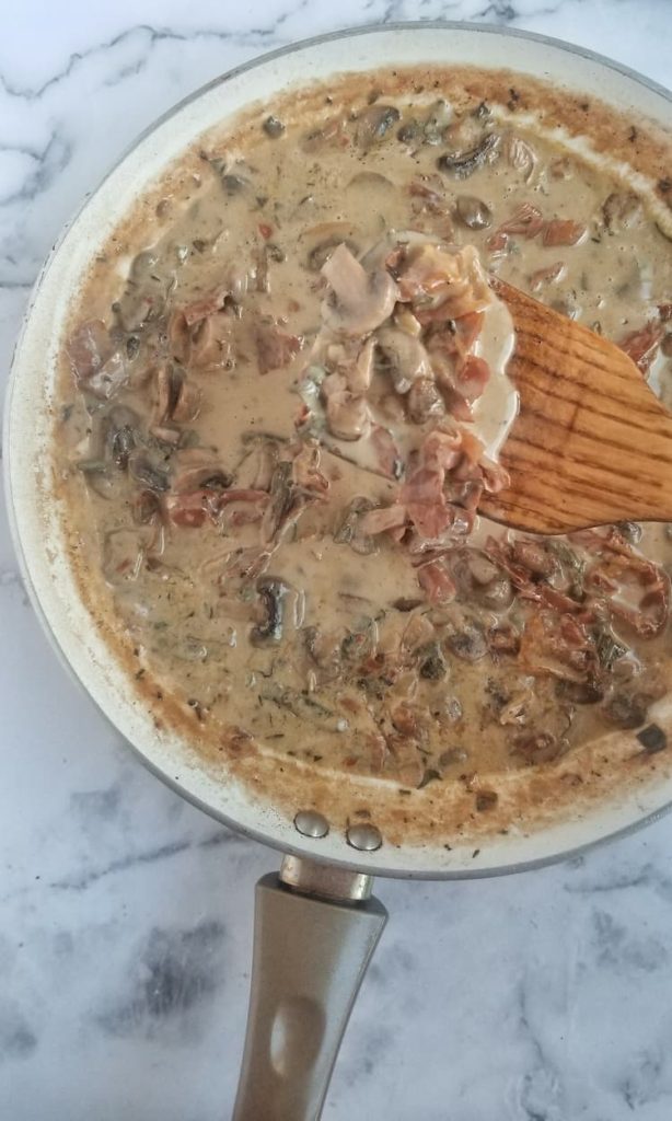 skillet with mushroom, prosciutto and herb cream sauce with a spatula picking some up
