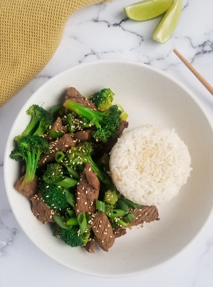bowl of beef and broccoli with rice, 2 lime wedges in the background