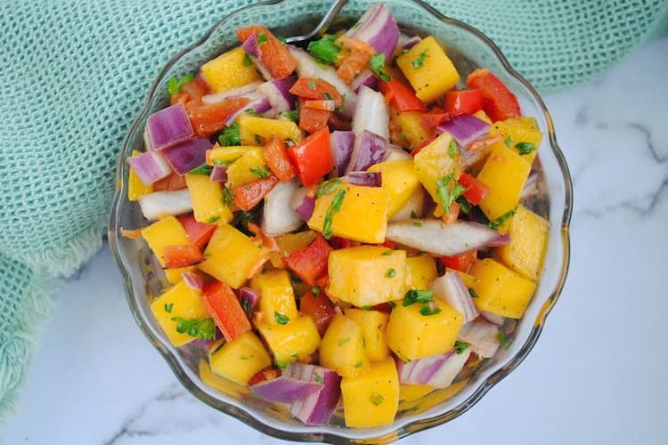 chunks of mango, red onion, parsley, red pepper and habaneros in a small glass bowl