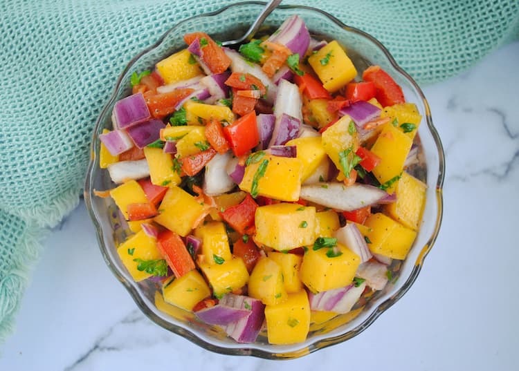 chunks of mango, red onion, parsley, red pepper and habaneros in a small glass bowl