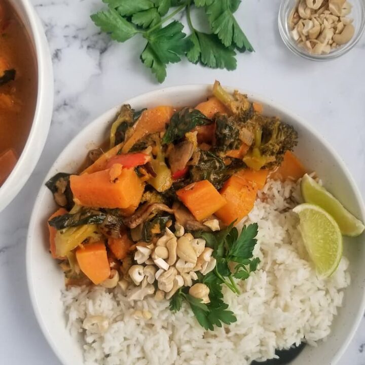 bowl of cubed sweet potato with other veggies such as spinach and sliced mushrooms, rice, parsley, chopped cashews and sliced lime, spoon in the bowl, fresh bunch of parsley and bowl of rice in the background, small bowl of cashews in the background