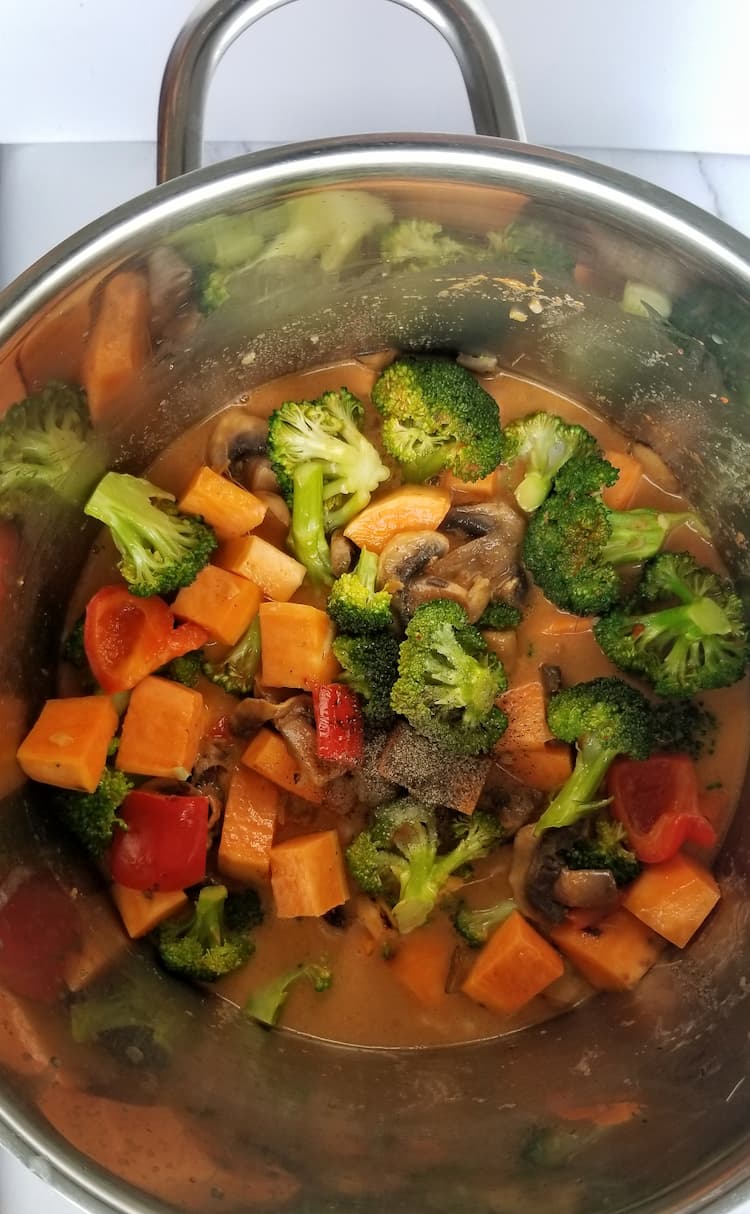 pot of cubed sweet potatoes, red pepper chunks, sliced mushrooms and broccoli florets in an orange broth