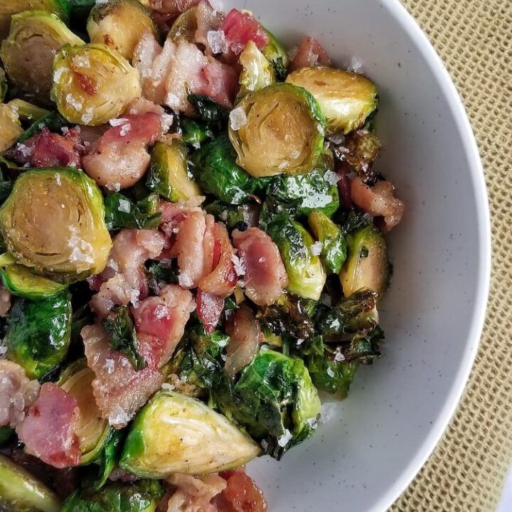 close up of a big bowl of cooked brussel sprouts baked with bacon and maple syrup, on a yellow cloth
