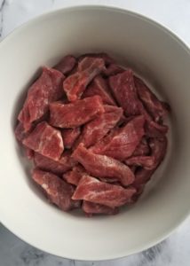 plain raw steak strips in a white bowl