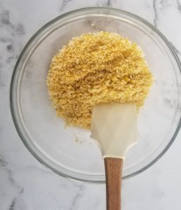 clear bowl of nutritional yeast and breadcrumbs with a white rubber spatula inside