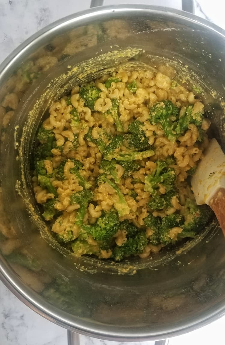 silver pot of vegan mac and cheese mixed with broccoli and cheese sauce, white rubber spatula inside
