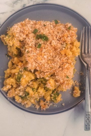 grey plate with generous portion of vegan mac and cheese with broccoli topped with breadcrumbs, two forks on the side