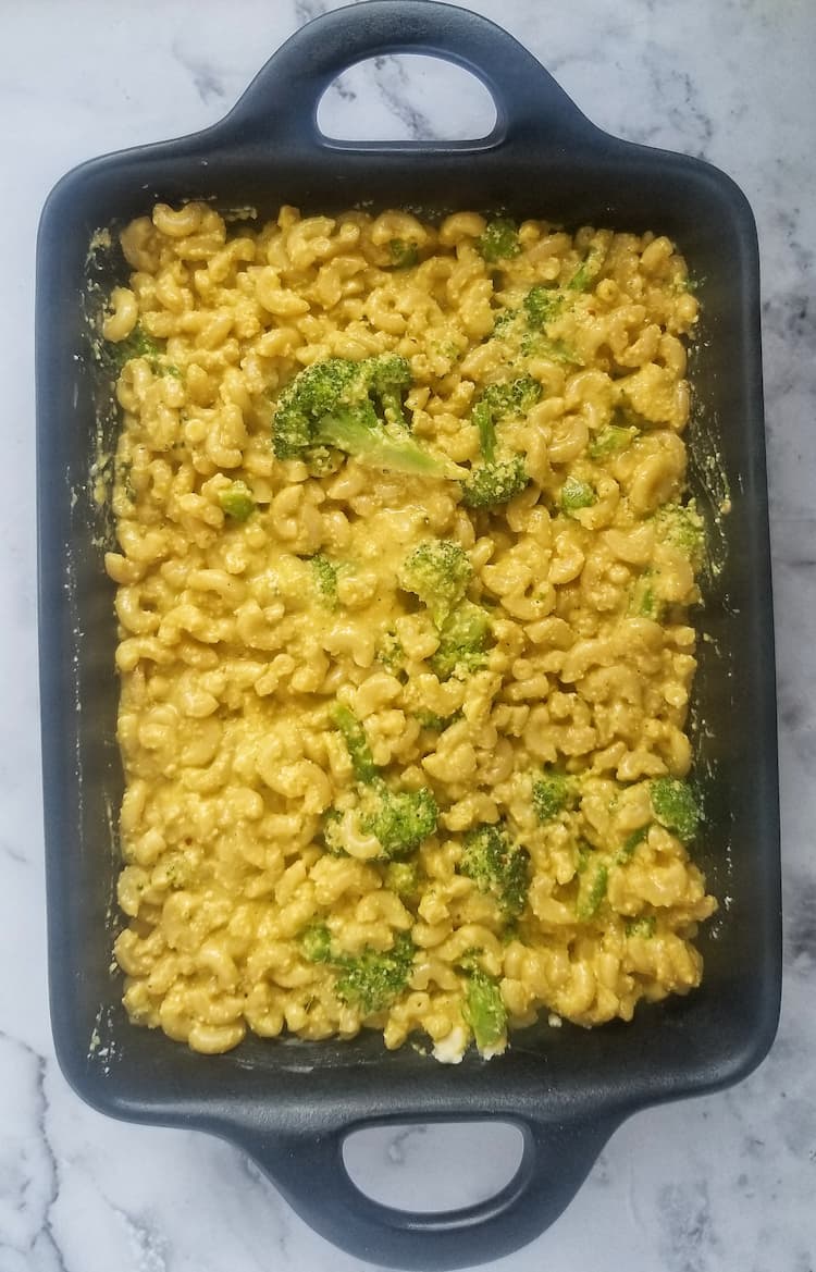 black cast iron casserole dish filled with elbow macaroni, cheese sauce and broccoli florets