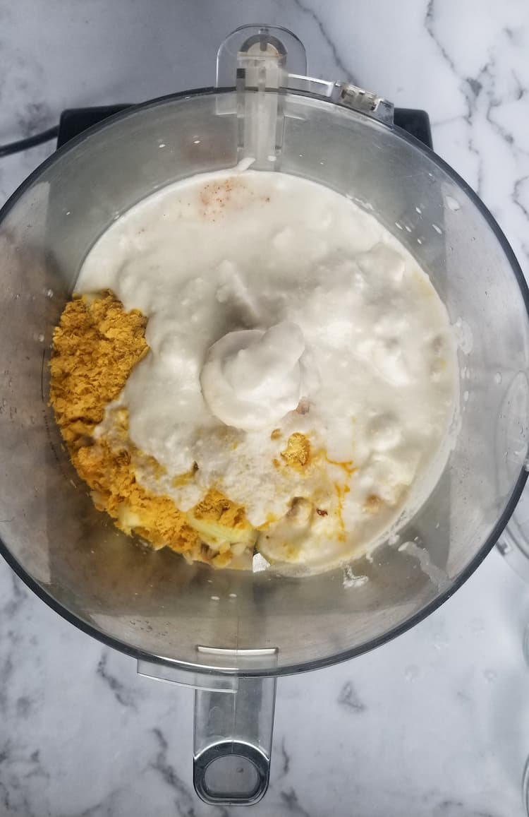 base of food processor filled with coconut milk, nutritional yeast and other ingredients