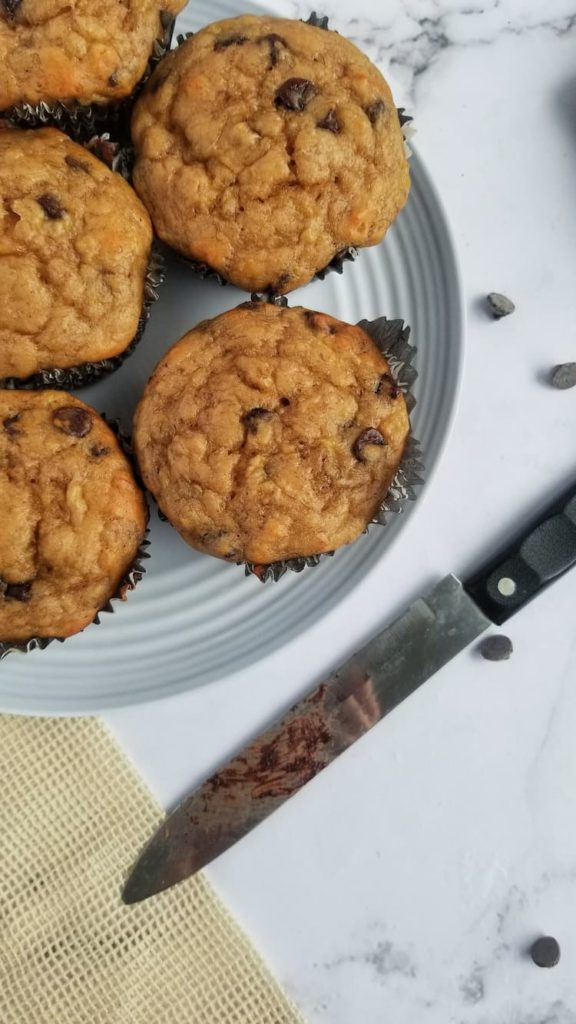plate of 5 freshly baked chocolate chip muffins next to a knife with chocolate on it