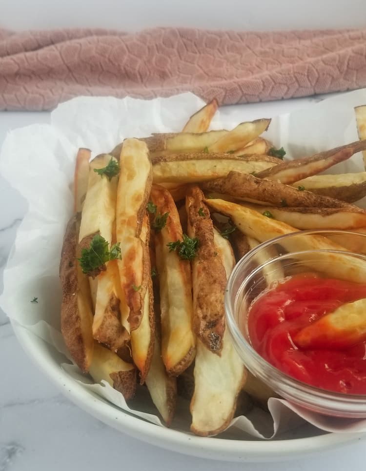 side view of bow of air fryer fries with ketchup and chopped parsley