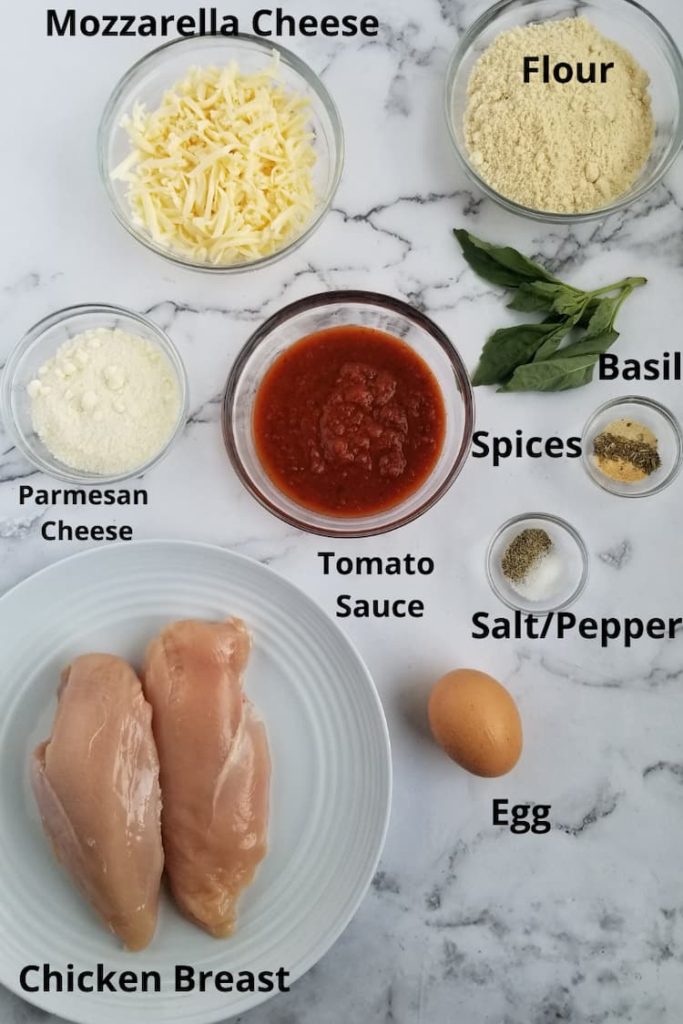ingredients for easy chicken parmesan - chicken breast, tomato sauce, mozzarella cheese, parmesan cheese, flour, an egg, salt and pepper, spices, fresh basil