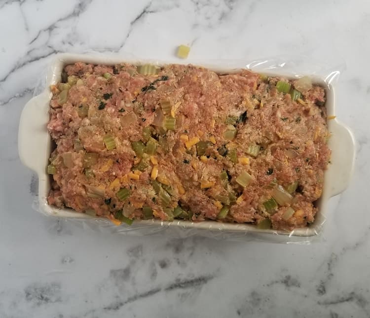 loaf pan with plastic wrap and an uncooked meatloaf inside