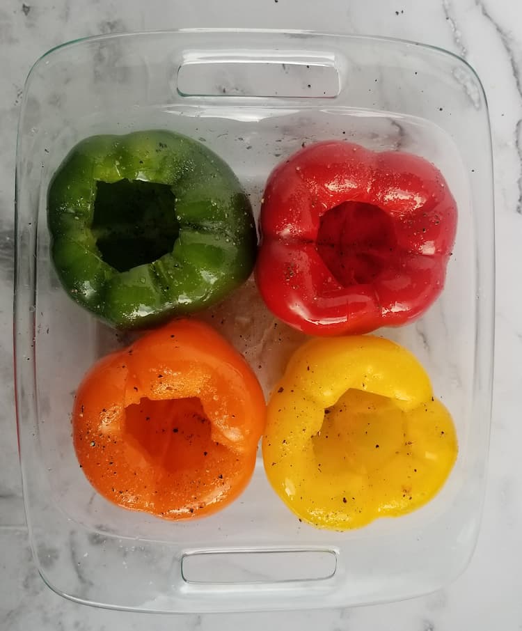 casserole dish with 4 hollow bell peppers, 1 red, 1 yellow, 1 orange and 1 green, salt and pepper on them with oil