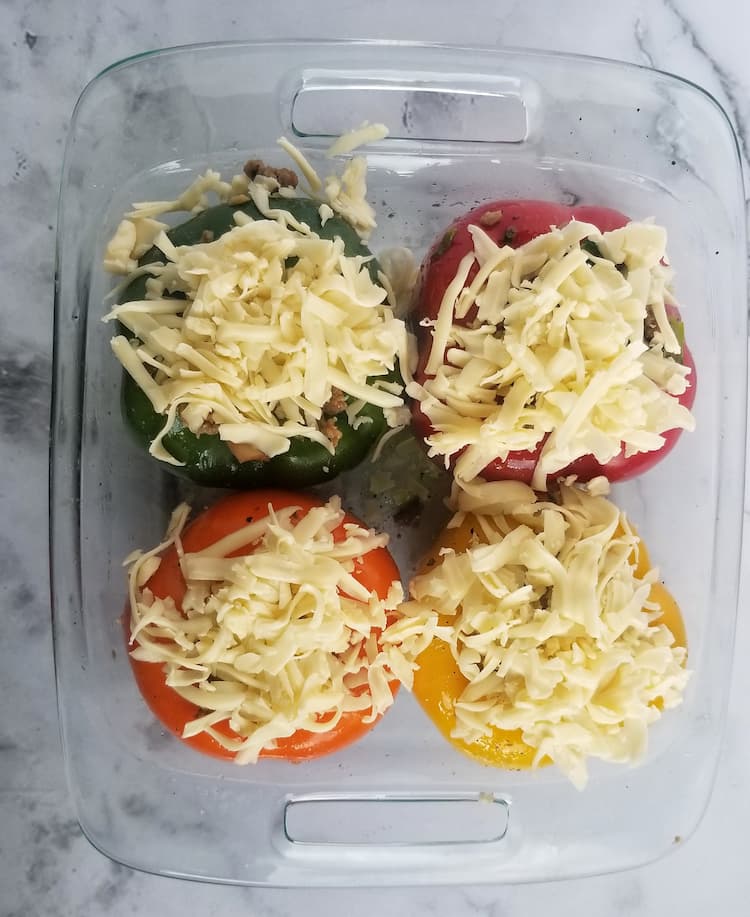 casserole dish with 4 stuffed peppers, 1 green, 1 yellow, 1 red, 1 orange, topped with unmelted mozzarella cheese