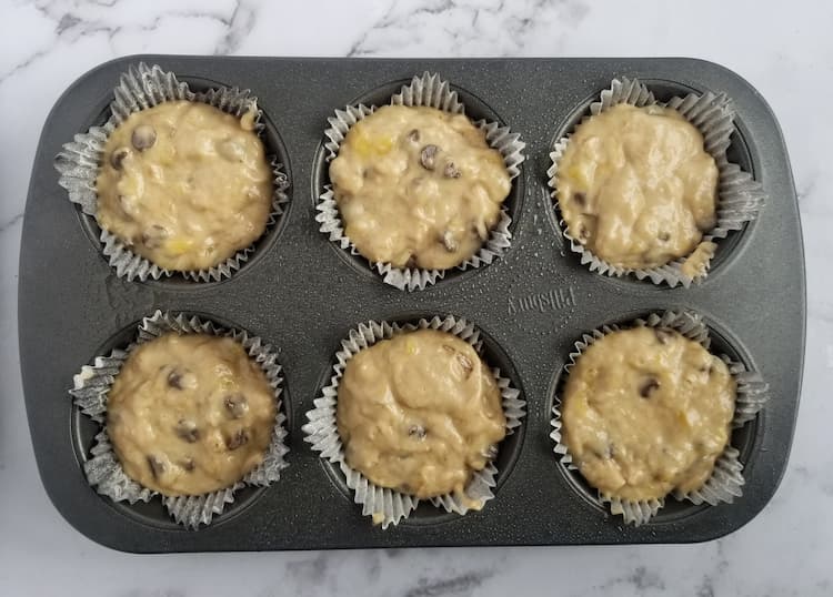 6 slot muffin tin filled with muffin batter that has chocolate chips and lined with muffin liners