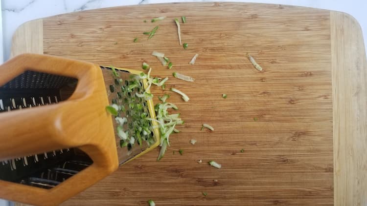 cutting board, box grater and some shredded cucumber