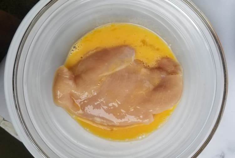 a bowl with a beaten egg and a raw chicken breast inside