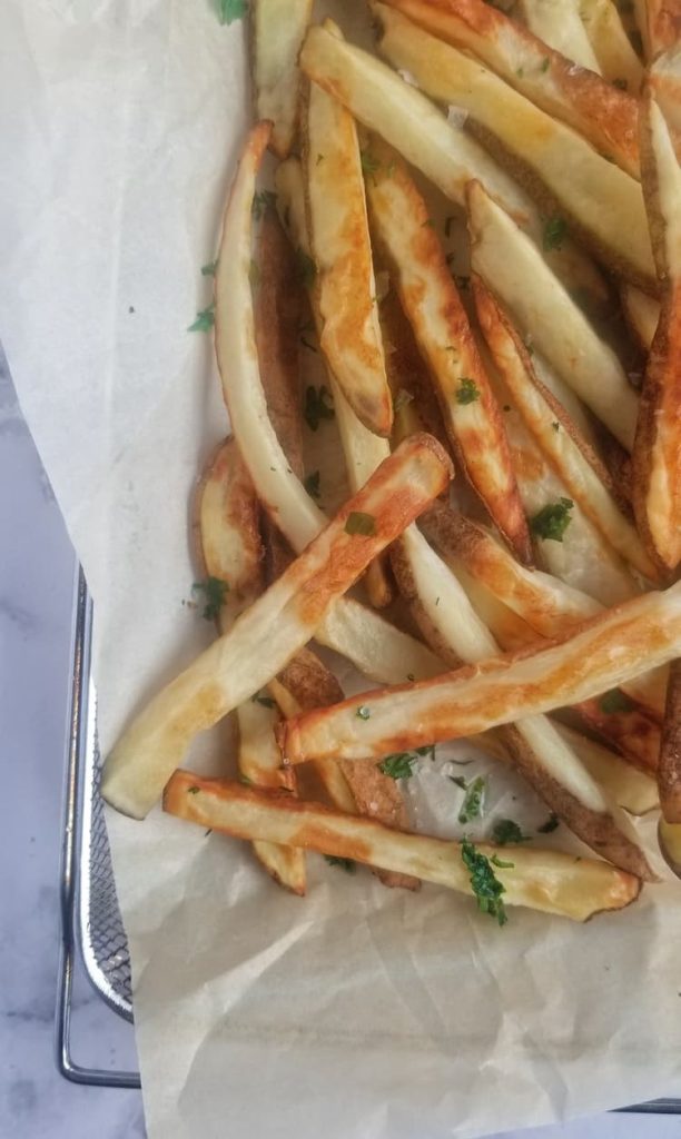 corner view of air fryer fries on a brown parchment paper, topped with parsley