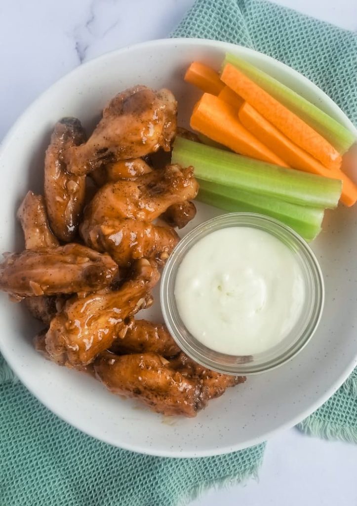 bowl of honey garlic chicken wings with blue cheese dip and celery and carrot sticks