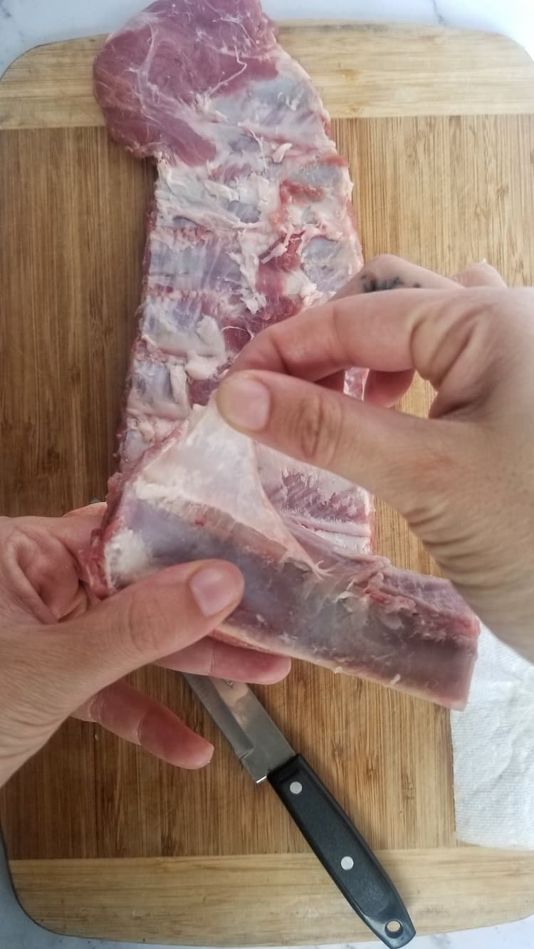 hand pulling the membrane off the back of a rack of pork ribs