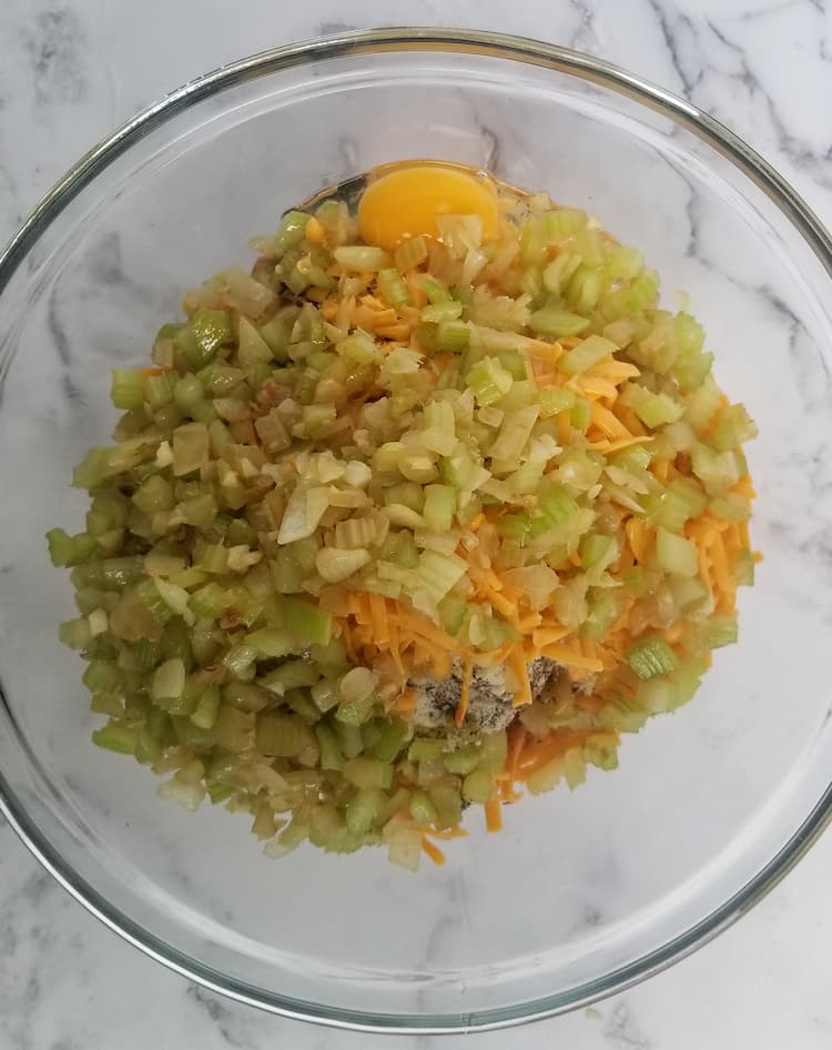 bowl of ingredients for keto meatloaf before mixing - you can see sauteed onions and celery, an egg and grated cheddar cheese